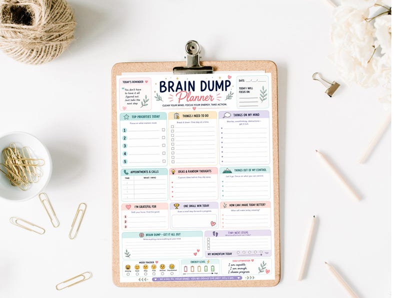 Puede incluir: Una hoja de Brain Dump Planner sujeta en un portapapeles de corcho marr&oacute;n. El planificador incluye secciones para prioridades, listas de tareas, citas, gratitud y seguimiento del estado de &aacute;nimo, con encabezados en tonos pastel.