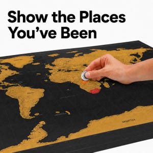 Puede incluir: Un mapa del mundo para rascar de color negro con continentes dorados y el texto "Show the Places You've Been" en la parte superior. El mapa presenta una zona parcialmente rascada en África que revela un color rojo bajo la lámina dorada.
