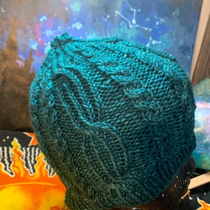 May include: Teal blue knitted hat with a cable knit pattern.
