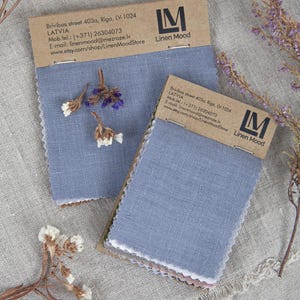 Puede incluir: Dos muestras de tela de lino azul con encabezados de cartón marrón que muestran el logotipo de Linen Mood e información de contacto. El texto incluye la dirección Brivibas street 403a, Riga, LV-1024, Letonia. Las medidas son 6,5x10 cm y 10x10 cm.
