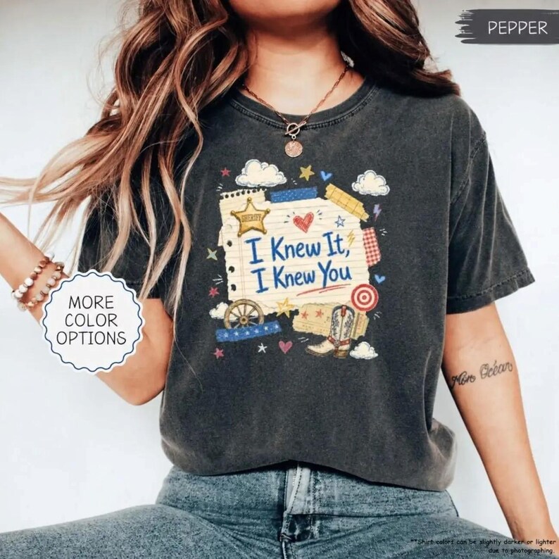 Puede incluir: Una camiseta gris carb&oacute;n de manga corta con un estampado gr&aacute;fico de una p&aacute;gina de bloc de notas con el texto I Knew It, I Knew You. El dise&ntilde;o incluye ilustraciones de una estrella de sheriff, un coraz&oacute;n, una rueda, una bota y una diana.