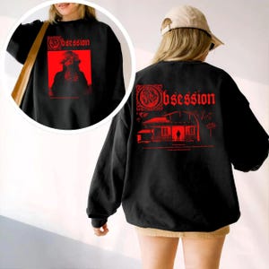 May include: A black long-sleeve sweatshirt featuring a red graphic print. The back displays a house illustration with the text "Obsession" and a silhouette figure. The front chest area shows a smaller red graphic with the same text "Obsession".