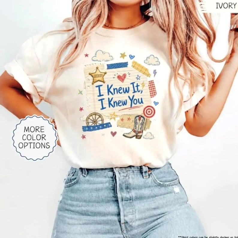 Puede incluir: Una camiseta de manga corta color marfil con un estampado gr&aacute;fico que incluye el texto I Knew It, I Knew You. El dise&ntilde;o presenta una estrella de sheriff, un coraz&oacute;n rojo, una rueda de carreta, una bota vaquera, una diana y estrellas y nubes.