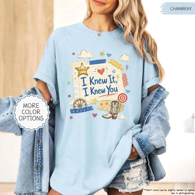 Puede incluir: Una camiseta de manga corta azul claro con un estampado gr&aacute;fico de una p&aacute;gina de bloc de notas rayada con el texto I Knew It, I Knew You, una estrella de sheriff, una bota vaquera, una rueda de carreta, un coraz&oacute;n y estrellas y nubes.