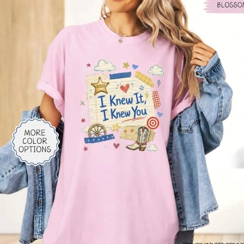 Puede incluir: Una camiseta rosa claro con un estampado gr&aacute;fico de una hoja de papel rayado con el texto I Knew It, I Knew You. El dise&ntilde;o incluye una estrella de sheriff dorada, un coraz&oacute;n rojo, una rueda de carreta, una bota vaquera y varias estrellas y nubes.