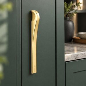 May include: A vertical gold-toned metal cabinet handle with a curved top section and a straight lower body. The handle features a smooth, polished finish and the word Ryland is engraved in a script font near the bottom edge.