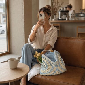 Puede incluir: Una camisa blanca de botones, pantalones vaqueros azul claro y un bolso de ganchillo en tonos azul claro y crema con un asa de cuentas de madera. El bolso contiene un peque&ntilde;o ramo de tulipanes amarillos. Una taza de cer&aacute;mica blanca sobre una mesa.