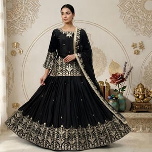 May include: A black embroidered dress with a matching scarf. The dress features gold embroidery on the bodice, sleeves, and hem. The background has a decorative pattern.