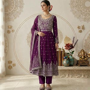 May include: A plum-colored, long-sleeved salwar kameez with intricate silver embroidery. The ensemble includes matching pants and a dupatta. The dress features a detailed bodice and hemline, creating an elegant look. The outfit is suitable for special occasions.