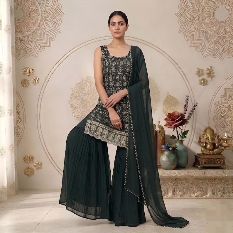 May include: A dark green sleeveless tunic featuring intricate gold floral embroidery and a scalloped hem, paired with matching wide-leg pleated trousers and a sheer, lightweight dupatta draped over one shoulder, creating a coordinated ensemble.