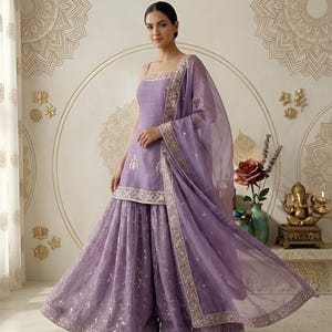 May include: A lavender-colored, formal ensemble featuring a sleeveless top and wide-leg pants. The outfit includes a matching sheer scarf with decorative trim. The ensemble is embellished with gold accents and embroidery, creating an elegant look.