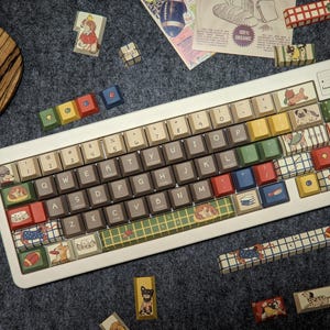 May include: A white mechanical keyboard featuring a custom keycap set with various dog illustrations, plaid patterns, and solid colored keys in red, blue, green, and yellow. The keys include alphanumeric characters and symbols with a dog-themed aesthetic.