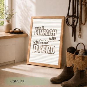 Könnte beinhalten: Ein gerahmter Druck mit dem deutschen Text "Wenn es einfach wäre, wäre es kein Pferd" (Wenn es einfach wäre, wäre es kein Pferd). Der Druck ist in einem hellen Holzrahmen mit gestreiftem Hintergrund. Braune Stiefel und Reitausrüstung.