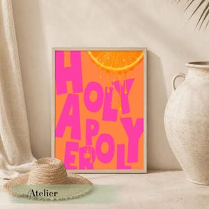 Könnte beinhalten: Ein gerahmter Kunstdruck mit den Worten "HOLY APOLOGY" in leuchtend pinkfarbenen Buchstaben auf orangefarbenem Hintergrund. Oben ist eine Orangenscheibe mit tropfendem Saft. Ein Strohhut befindet sich im Vordergrund.