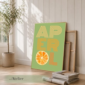 Könnte beinhalten: Gerahmtes Poster mit dem Wort "APEROL" in orangefarbenen und beigefarbenen gestreiften Buchstaben auf grünem Hintergrund. Unter den Buchstaben befindet sich eine Orangenscheibe. Das Poster lehnt an einer Wand neben einer Topfpflanze.