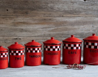 May include: Six red enamel canisters with black and white checkered lids. The canisters are labeled "POIVRE", "THE", "TAPIOCA", "CHICOREE", "CAFE", and "SUCRE".