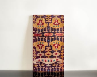 Könnte beinhalten: Ein rechteckiges Stück Stoff mit einem sich wiederholenden Muster aus geometrischen Formen in den Farben Lila, Rot, Gelb und Blau.