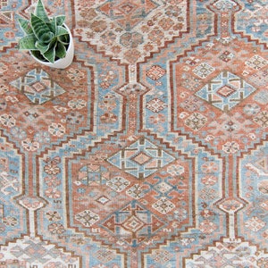 Puede incluir: Una alfombra vintage con un patr&oacute;n geom&eacute;trico en tonos azules, marrones y rosas. La alfombra tiene un medall&oacute;n central y un borde con un dise&ntilde;o repetitivo.