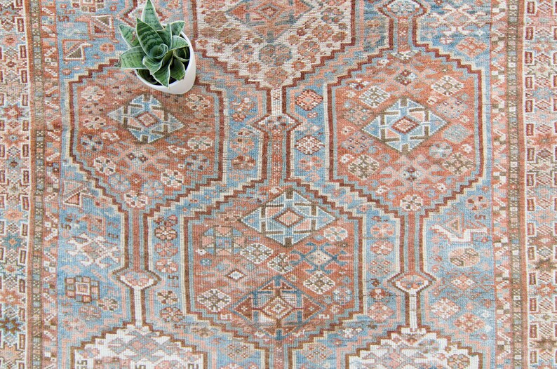 Puede incluir: Una alfombra vintage con un patr&oacute;n geom&eacute;trico en tonos azules, marrones y rosas. La alfombra tiene un medall&oacute;n central y un borde con un dise&ntilde;o repetitivo.