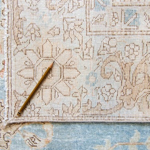 Op de afbeelding: Een close-up van een lichtblauw en beige gestreept tapijt met een houten potlood erop.