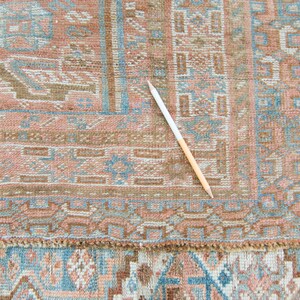 Puede incluir: Primer plano de una alfombra vintage con un patr&oacute;n geom&eacute;trico detallado en tonos marrones, azules y rosas. La alfombra tiene un borde de flecos y est&aacute; en buen estado.
