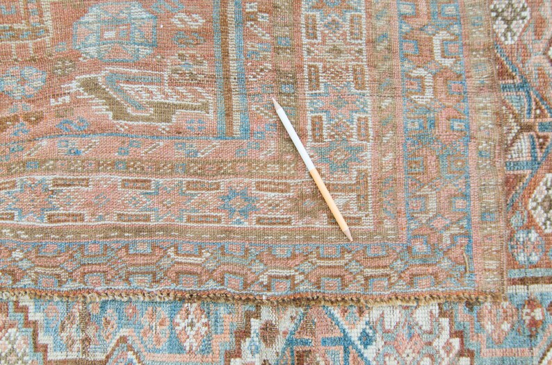 Puede incluir: Primer plano de una alfombra vintage con un patr&oacute;n geom&eacute;trico detallado en tonos marrones, azules y rosas. La alfombra tiene un borde de flecos y est&aacute; en buen estado.