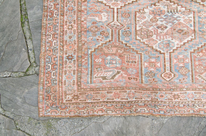 Puede incluir: Una alfombra vintage con un dise&ntilde;o persa tradicional. La alfombra tiene un fondo azul claro con un medall&oacute;n central en tonos de rosa, marr&oacute;n y blanco. La alfombra tiene un borde con flecos.