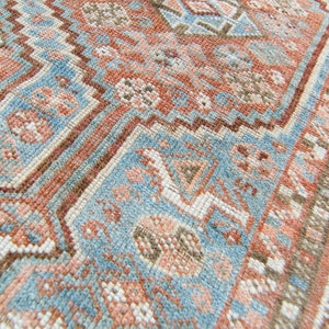 Puede incluir: Primer plano de una alfombra de patrones azules y rosas con intrincados dise&ntilde;os tejidos. La alfombra tiene un aspecto descolorido y vintage y est&aacute; hecha de un material suave y texturizado.