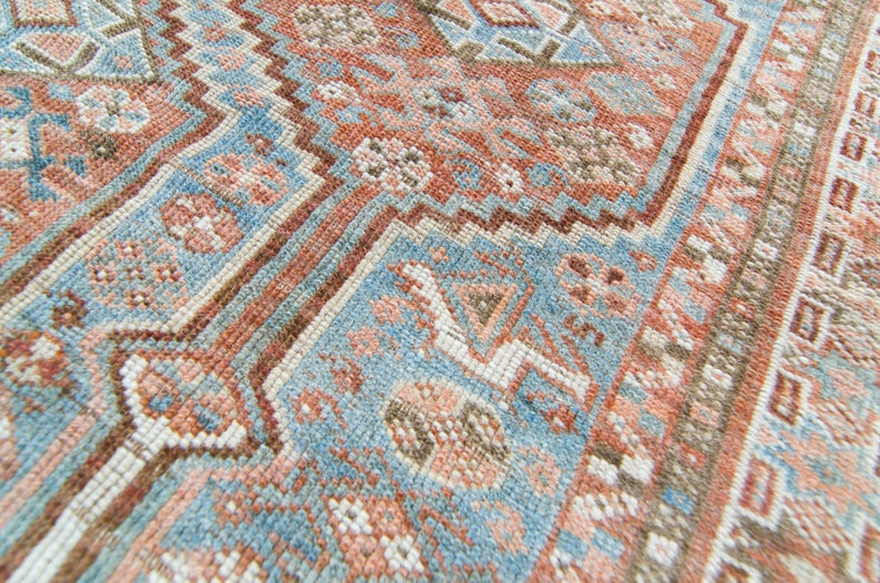 Puede incluir: Primer plano de una alfombra de patrones azules y rosas con intrincados dise&ntilde;os tejidos. La alfombra tiene un aspecto descolorido y vintage y est&aacute; hecha de un material suave y texturizado.