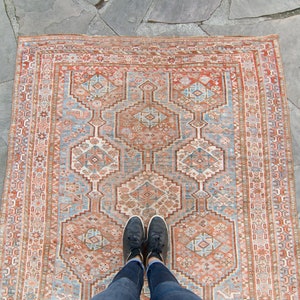 Puede incluir: Una alfombra vintage con un patr&oacute;n geom&eacute;trico en tonos rojos, azules y blancos. La alfombra tiene un aspecto desgastado y descolorido, y los colores son apagados. La alfombra est&aacute; colocada sobre una superficie de piedra.
