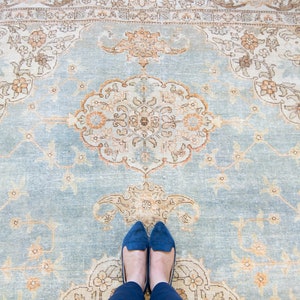 Op de afbeelding: Een blauw tapijt met een beige patroon van bloemenmotieven. Twee blauwe schoenen liggen op het tapijt.