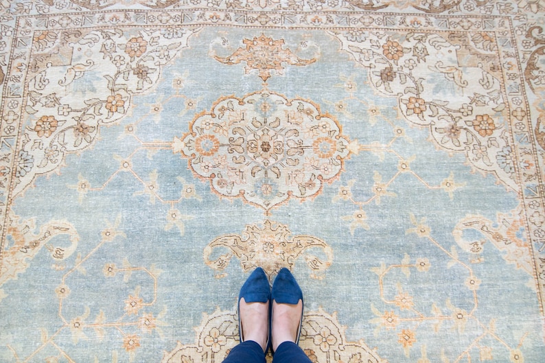 Op de afbeelding: Een blauw tapijt met een beige patroon van bloemenmotieven. Twee blauwe schoenen liggen op het tapijt.