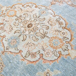 Op de afbeelding: Een vintage tapijt met een lichtblauwe achtergrond en een centraal medaillon in beige, bruin en perzikkleuren. Het medaillon heeft ingewikkelde bloem- en geometrische patronen.