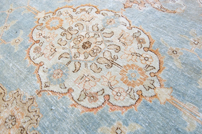 Op de afbeelding: Een vintage tapijt met een lichtblauwe achtergrond en een centraal medaillon in beige, bruin en perzikkleuren. Het medaillon heeft ingewikkelde bloem- en geometrische patronen.
