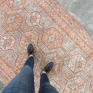 Puede incluir: Una alfombra vintage con un patr&oacute;n geom&eacute;trico en tonos rosa, azul y blanco. La alfombra est&aacute; colocada sobre un suelo de piedra.