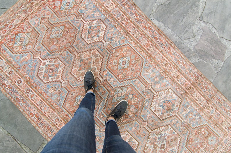 Puede incluir: Una alfombra vintage con un patr&oacute;n geom&eacute;trico en tonos rosa, azul y blanco. La alfombra est&aacute; colocada sobre un suelo de piedra.