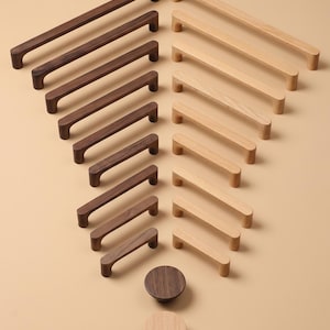 May include: A collection of wooden cabinet pulls and knobs in various sizes and shades of brown and light beige. The pulls are rectangular with rounded edges, and the knobs are circular. The items are arranged on a neutral background.