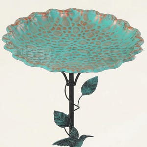 May include: A decorative bird bath with a turquoise-colored bowl and a bronze-colored rim. The bowl has a textured pattern. The bird bath is supported by a black metal pole with leaves and a hummingbird accent. The bird bath is approximately 20 inches in diameter.