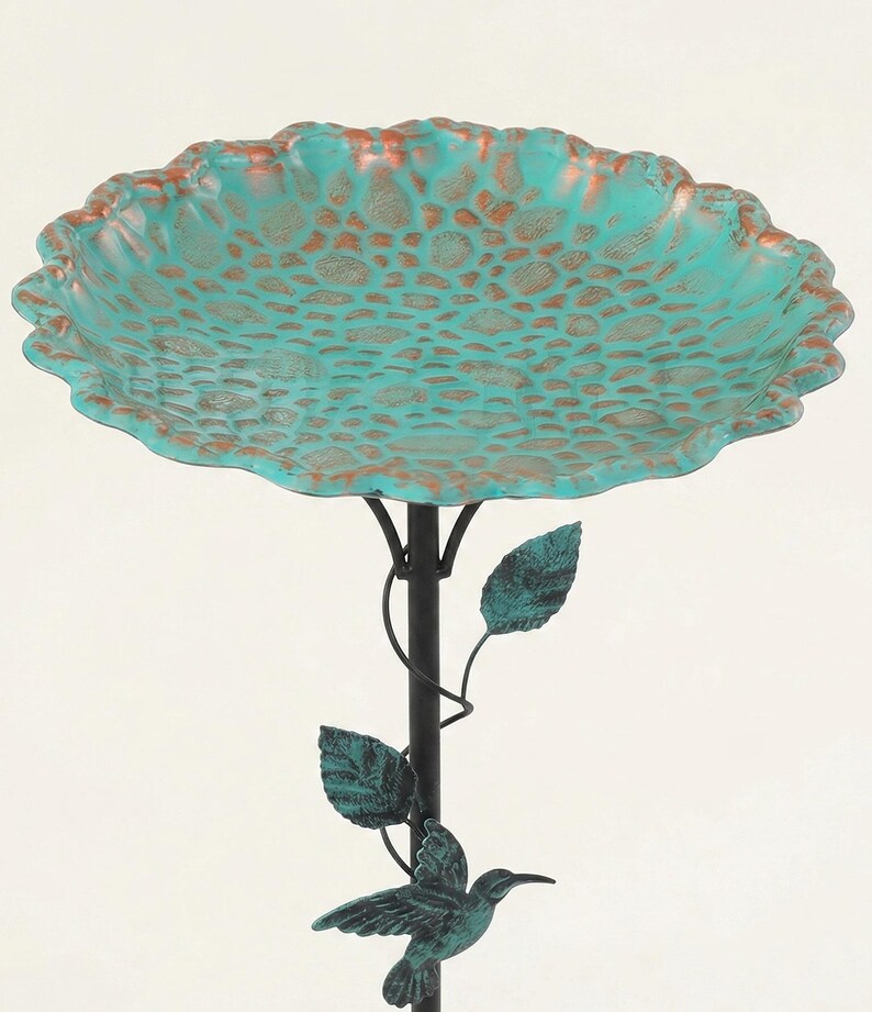 May include: A decorative bird bath with a turquoise-colored bowl and a bronze-colored rim. The bowl has a textured pattern. The bird bath is supported by a black metal pole with leaves and a hummingbird accent. The bird bath is approximately 20 inches in diameter.