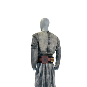 Puede incluir: Un conjunto de chaqueta de manga larga y falda a juego en color gris con un acabado desgastado y moteado. La chaqueta presenta un corte corto y paneles texturizados en los hombros. Un cintur&oacute;n negro ancho con un emblema cuadrado rojo central.