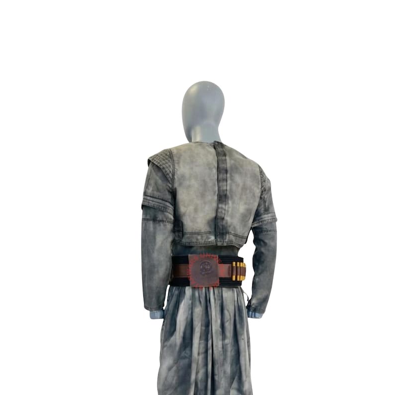 Puede incluir: Un conjunto de chaqueta de manga larga y falda a juego en color gris con un acabado desgastado y moteado. La chaqueta presenta un corte corto y paneles texturizados en los hombros. Un cintur&oacute;n negro ancho con un emblema cuadrado rojo central.