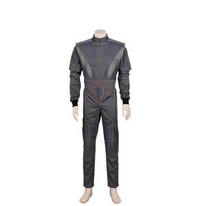 May include: A dark gray jumpsuit featuring a high collar, long sleeves with black cuffs, and a structured bodice with vertical stitching. The garment includes a geometric pattern on the lower sleeves and a red circular emblem on the front torso.