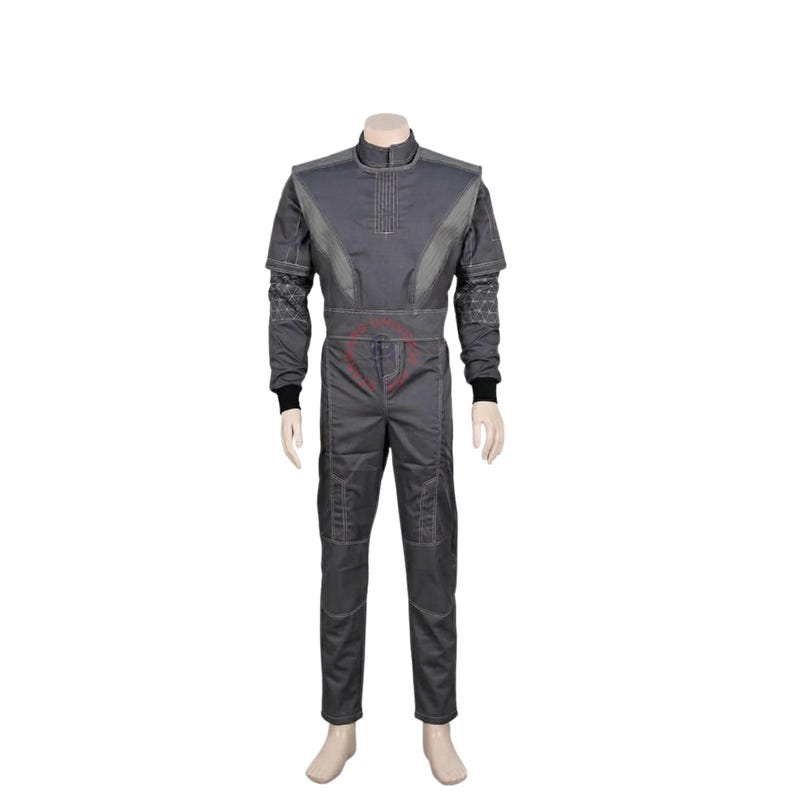 May include: A dark gray jumpsuit featuring a high collar, long sleeves with black cuffs, and a structured bodice with vertical stitching. The garment includes a geometric pattern on the lower sleeves and a red circular emblem on the front torso.