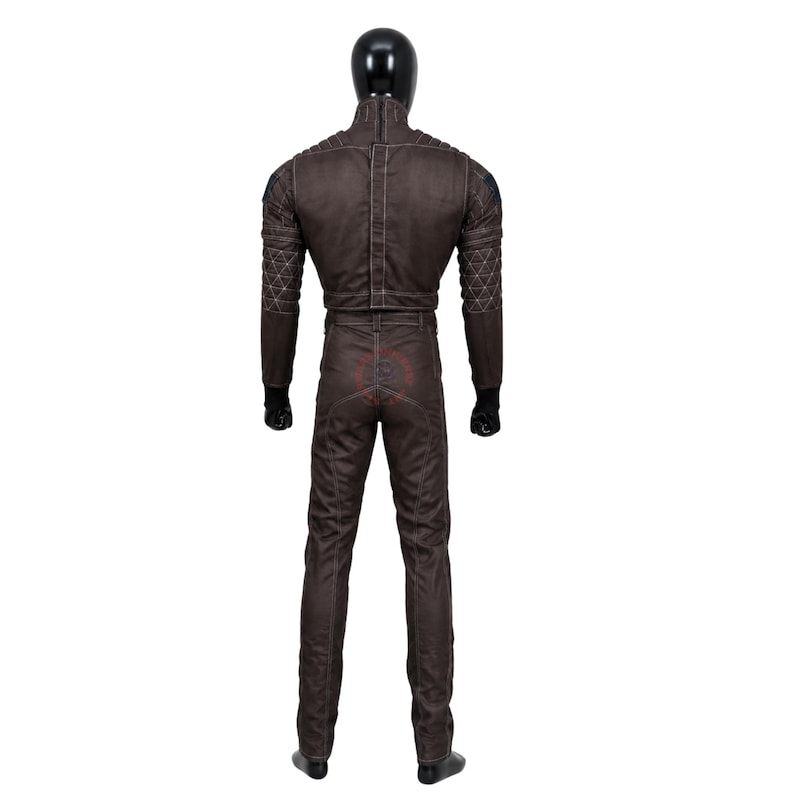 Puede incluir: Un mono de cuerpo entero de color marr&oacute;n oscuro sobre un maniqu&iacute;, con cuello alto, mangas largas con patrones triangulares acolchados en los antebrazos, costuras blancas visibles y una cintura ajustada con dise&ntilde;o de trabillas.
