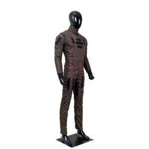 Puede incluir: Un mono de cuerpo entero de color marr&oacute;n sobre un maniqu&iacute; negro. La prenda presenta un cuello alto, mangas largas con pu&ntilde;os negros y parches rectangulares negros en el pecho, los hombros y los muslos. La tela tiene costuras visibles.