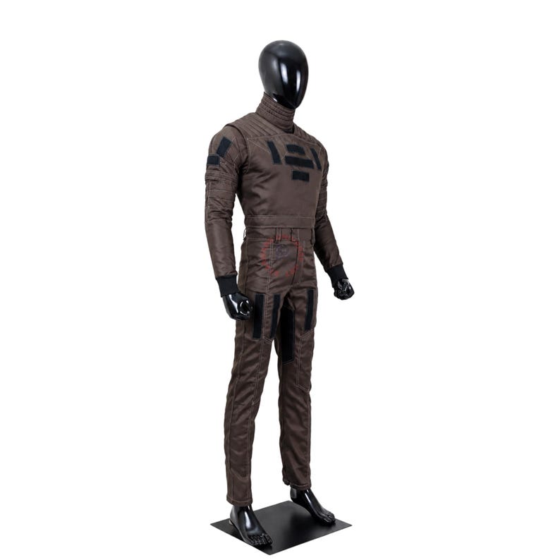 Puede incluir: Un mono de cuerpo entero de color marr&oacute;n sobre un maniqu&iacute; negro. La prenda presenta un cuello alto, mangas largas con pu&ntilde;os negros y parches rectangulares negros en el pecho, los hombros y los muslos. La tela tiene costuras visibles.