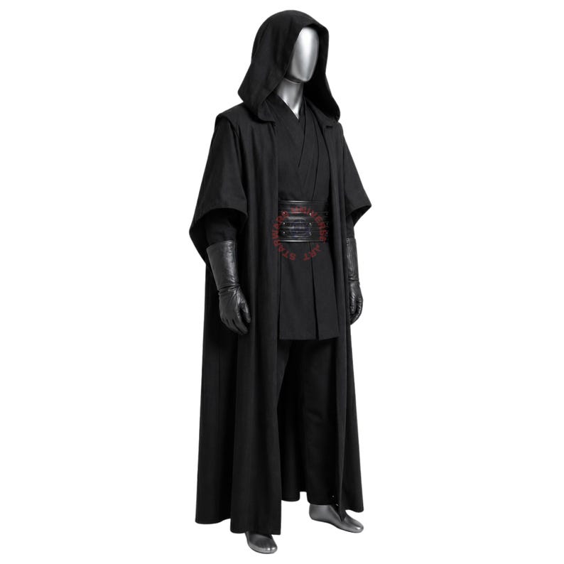 May include: A full-length black costume ensemble featuring a hooded cloak, a layered tunic, and matching trousers. The outfit includes a wide black belt with horizontal stitching and long black gloves. A silver-toned mannequin displays the attire.
