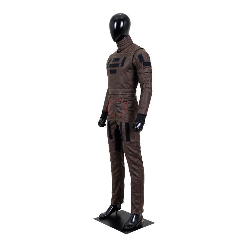 Puede incluir: Un mono t&aacute;ctico marr&oacute;n sobre un maniqu&iacute; negro, con cuello alto, mangas largas con pu&ntilde;os negros y parches rectangulares negros en el pecho y los brazos. El pantal&oacute;n incluye detalles de costuras rojas y paneles de tela negra adicionales.