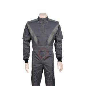 May include: A dark gray jumpsuit featuring a high collar, long sleeves with black cuffs, and a structured bodice with vertical stitching. The sleeves display a geometric triangular pattern, while the pants include reinforced knee panels and visible seams.