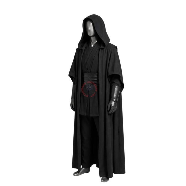 May include: A full-length black hooded robe worn over a matching black tunic and trousers. The outfit includes a wide black waist belt with horizontal stitching and long black gloves. A red circular logo is visible on the center of the waist belt.